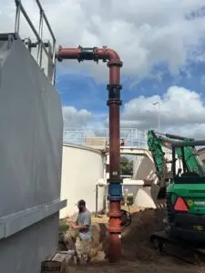 An outdoor wastewater treatment facility with large white tanks and ongoing pipe maintenance.