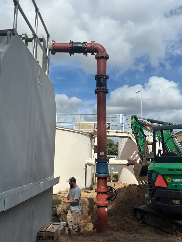 An outdoor wastewater treatment facility with large white tanks and ongoing pipe maintenance.