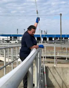 A CWS technician using a long sampling pole to test water at a treatment facility.