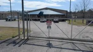 A metal gate with barbed wire and a no trespassing sign in front of a large building