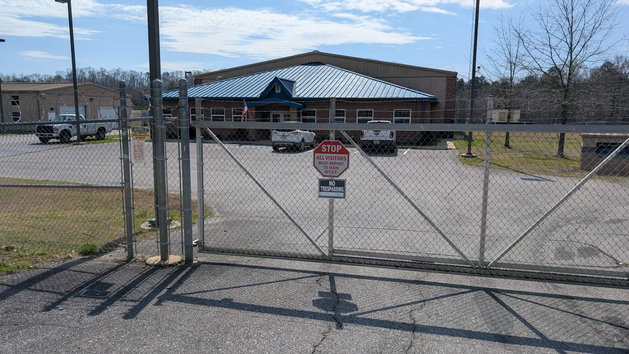 A metal gate with barbed wire and a no trespassing sign in front of a large building