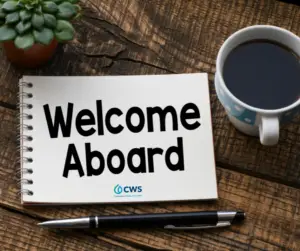 An image of "Welcome Aboard" with the CWS logo below written on a notepad. There is a succulent plant, a cup of coffee, and a ballpoint pen around the notepad.