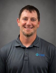Garrett Siemer Missouri Project Manager smiles wearing a gray collared shirt with CWS logo on it with a gray background.