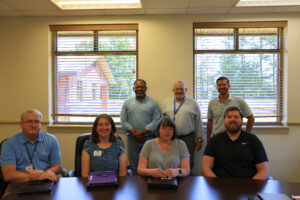 City officials and CWS employees sitting at a table and standing with two windows behind them